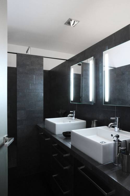 Carrelage noir intérieur de salle de bains moderne avec armoires en bois,  une baignoire blanche et un évier
